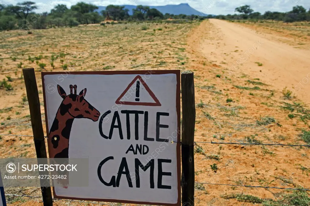 Africa, Namibia, Erongo Region. Where a dirt track bisects a bush farm, a sign on the road warns of the danger of speeding to cattle and game animals.