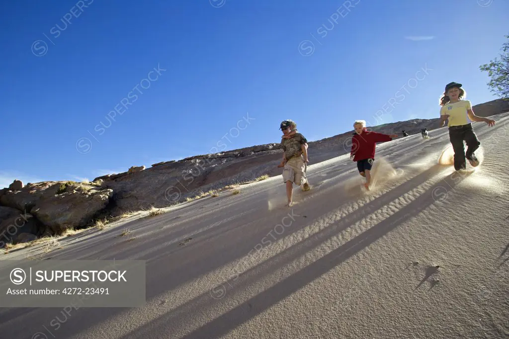 Namibia, Erongo Region, Brandberg Mountain. A group young of friends run down the steep face of a sand dune kicking up sand and enjoying themselves. (MR).