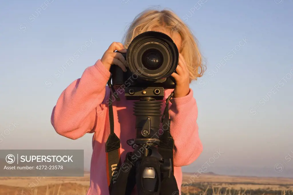 Namibia, Damaraland, Twfelfontien. A young girl takes photographs with a Canon camera mounted on a tripod at sunrise over the savannah near Twyfelfontien in northern Namibia (MR)