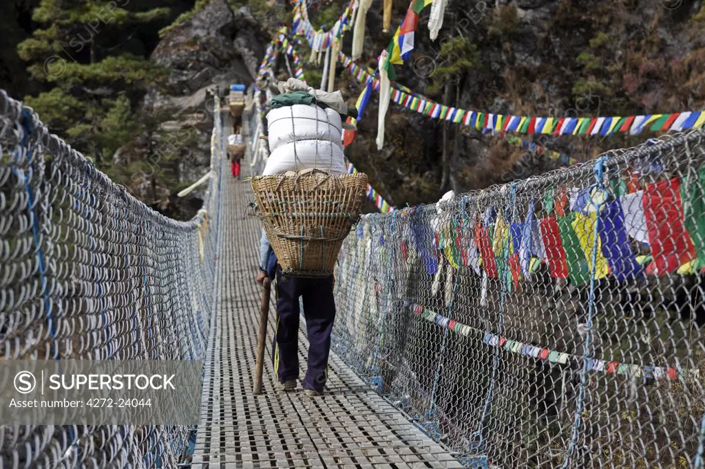 Nepal, Everest Region, Khumbu Valley. Heavily laden porters cross wire suspension bridge on the Everest Base Camp Trek near Namche Bazaar