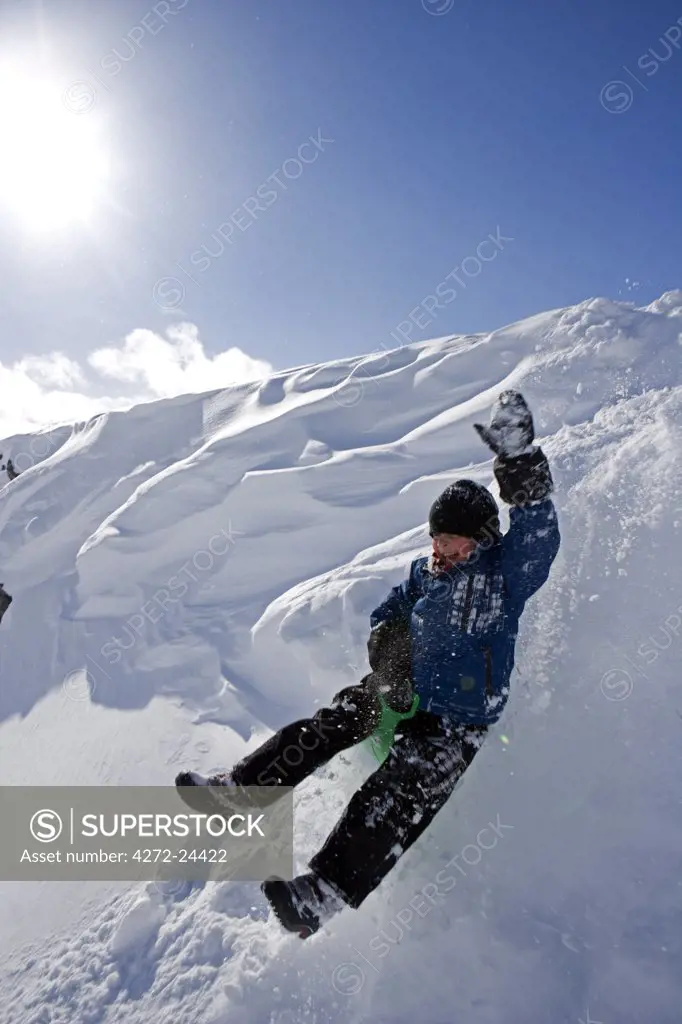 Norway, Tromso, Lyngen Alps.   Young boy has extreme fun tobogganing in bright winter son. (MR)
