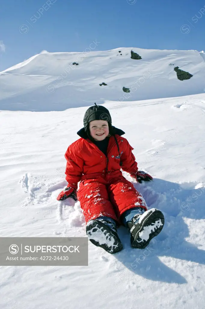 Norway, Tromso, Lyngen Alps.  A young girl dressed for the extreme cold in winter overalls plays in the snow. (MR)