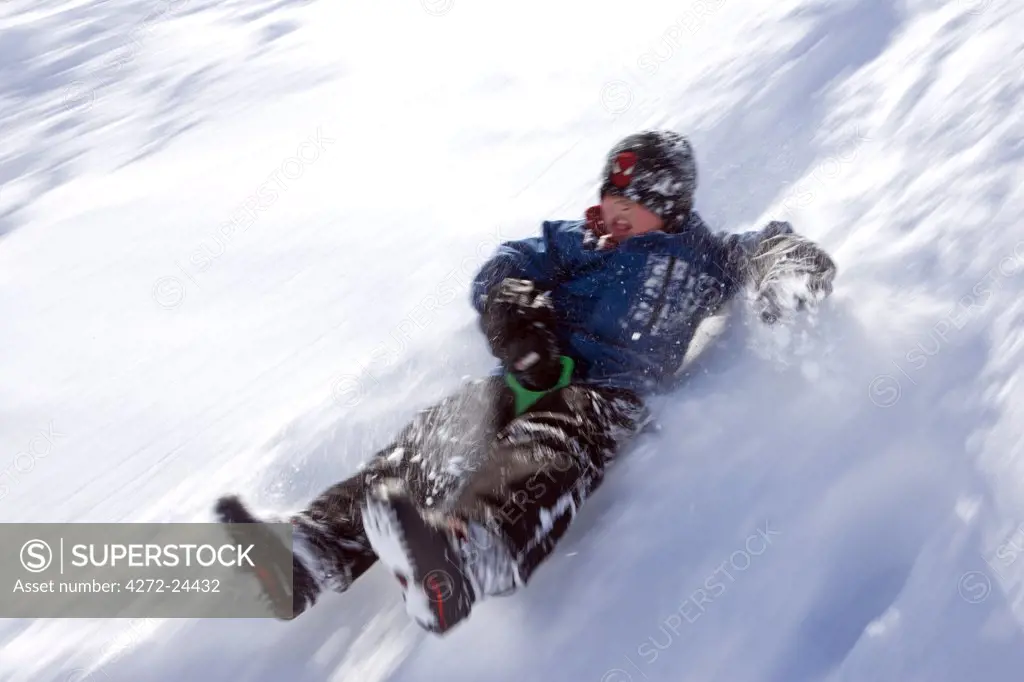 Norway, Tromso, Lyngen Alps. Young boy has extreme fun tobogganing in bright winter son. (MR)