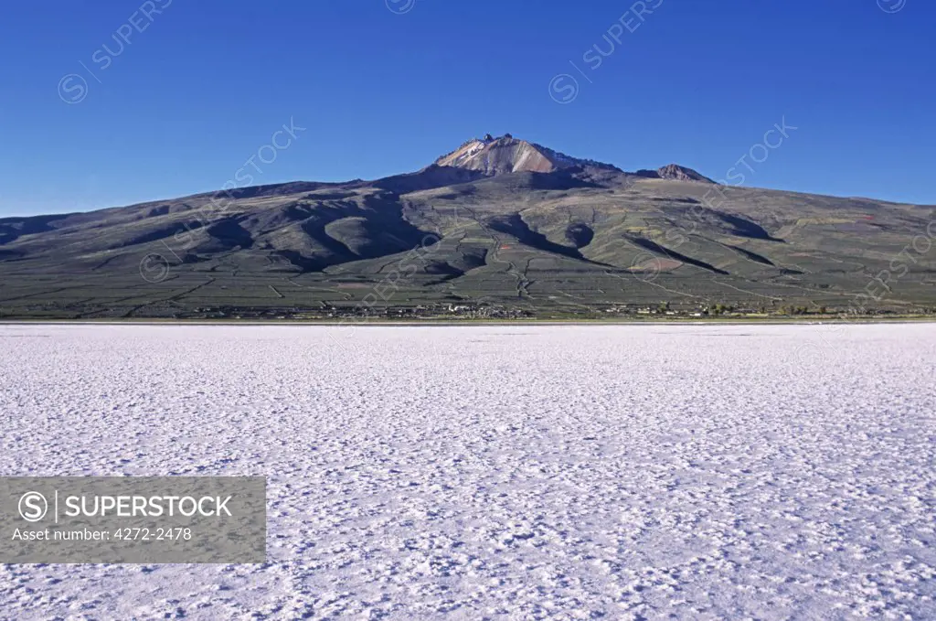 View across the great white expanse that is the Salar de Uyuni,  the largest salt flat in the world, towards village of Coquesa and towering above it the extinct volcano, Cerro Tunupa 5432m.  The lines on the slopes of Tunupa are drystone walls or pircas.