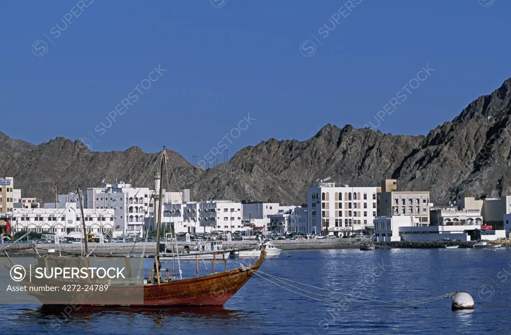 A wooden dhow moored in the harbour at Muttrah with the whitewashed apartment blocks and arid mountains behind