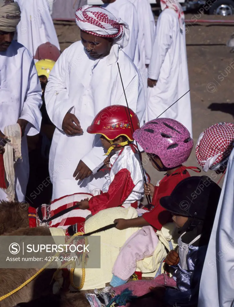 Jockeys wait in line on their mounts ready to be lead down to the start line at Al Shaqiyah camel race track. Jockeys can be as young as 4 years old.