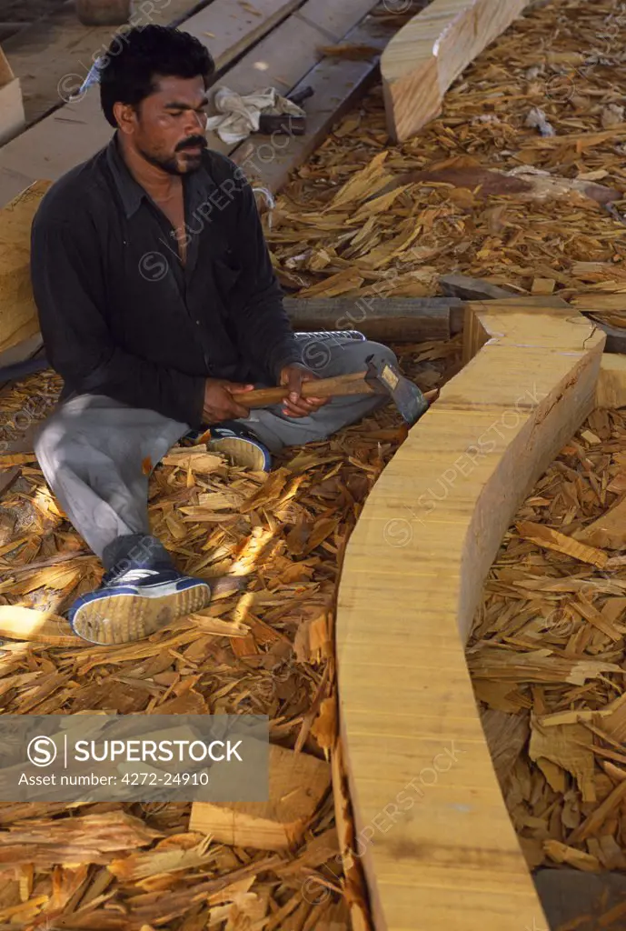 A craftsman uses an adze to shape the rib of a large dhow which is being built in the boat yard at Sur