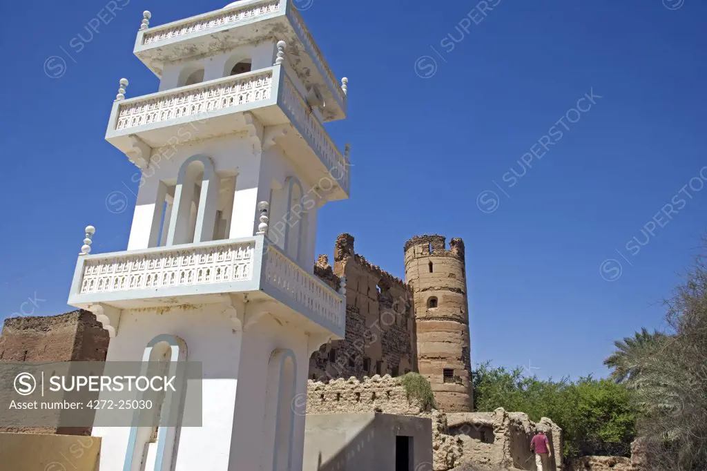 Oman, Batinah Plain, Rustaq. A small village mosque and minaret in front of an old crumbling fortified house.
