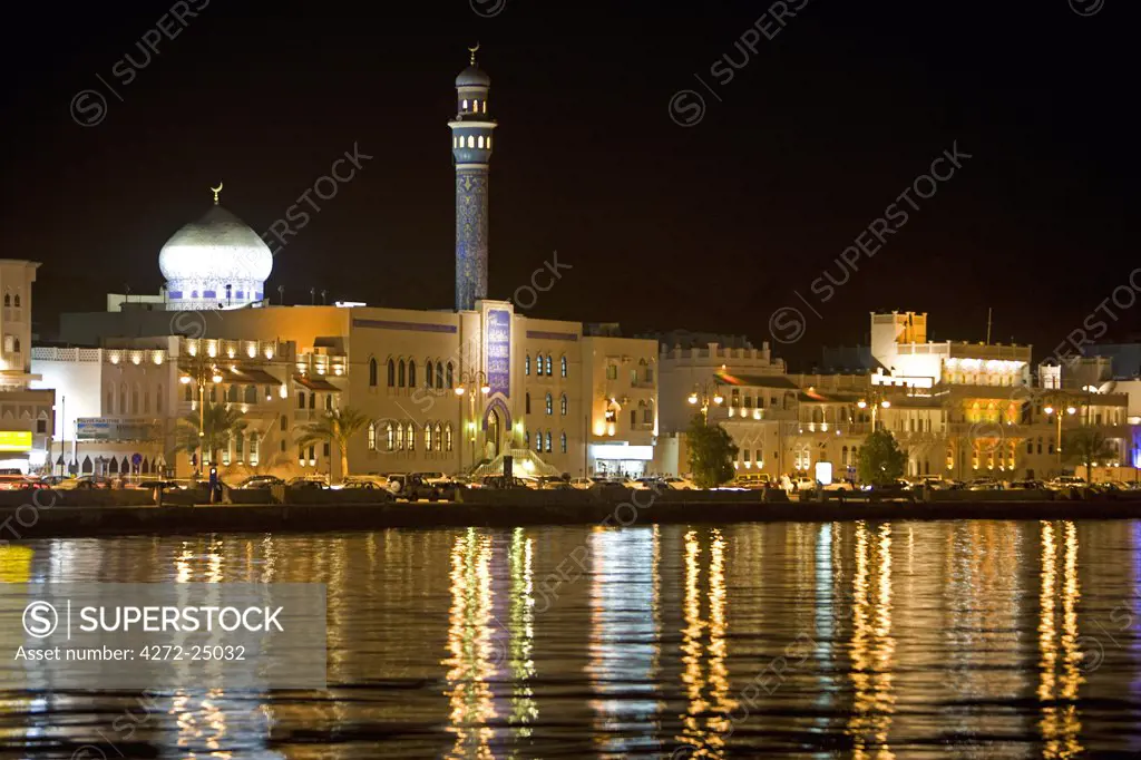 Oman, Muscat. Looking across the water to the brightly lit Corniche and the Mutrah Souq area of the countries capital, a traditional bazar the souq is a warren of alleyways and lined by traditional stalls.