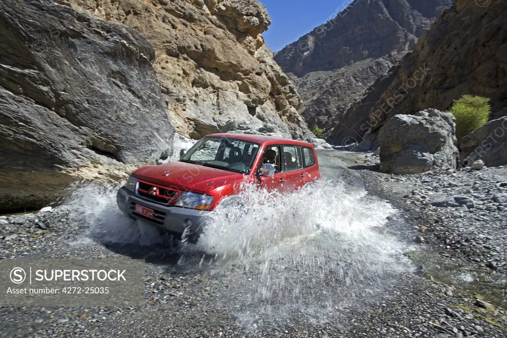 Oman, Western Hajar Mountains, Wadi Bani Awf. A four wheel drive makes it across yet another wadi river crossing to reach an interior village.