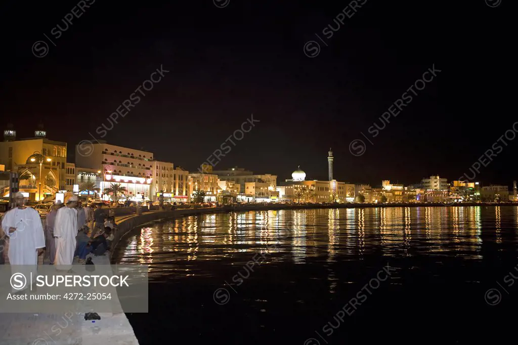 Oman, Muscat. Looking across the water to the brightly lit Corniche and the Mutrah Souq area of the countries capital, a traditional bazar the souq is a warren of alleyways and lined by traditional stalls.