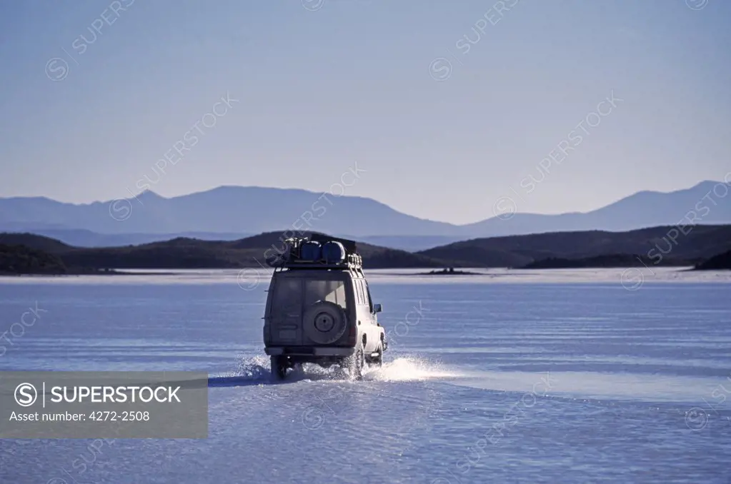 A tourist vehicle drives through surface water lying on top of the salt crust on the Salar de Coipasa