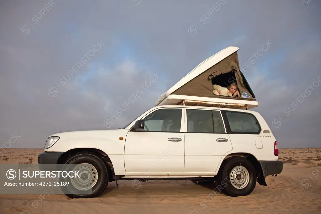 Oman, Wahiba Sands. A young lady peeps out from her roof-top tent early in the morning. MR