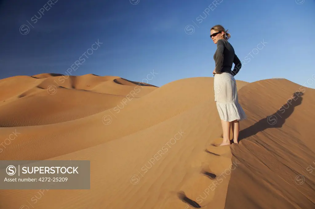 Oman, Empty Quarter. Oman, Empty Quarter. A young lady standing at the crest of a dune. MR.