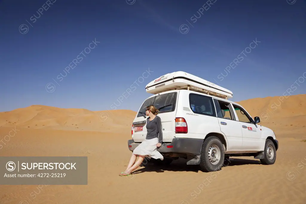 Oman, Empty Quarter. A young lady takes a break from driving to enjoy the views.