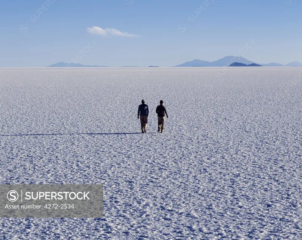 Two tourists walk across the endless salt crust  of the Salar de Uyuni, the largest salt flat in the world at over 12,000  square kilometres.