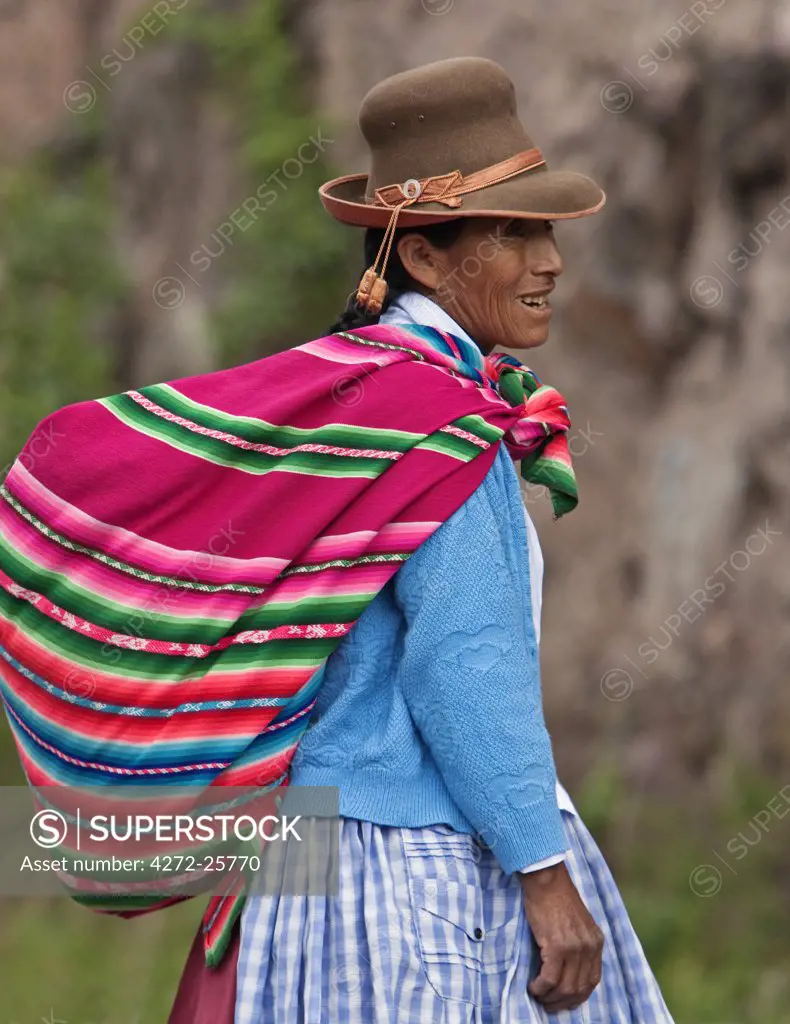 Peru. An Indian woman wearing a felt hat carries her farm produce to market in a brightly coloured blanket.