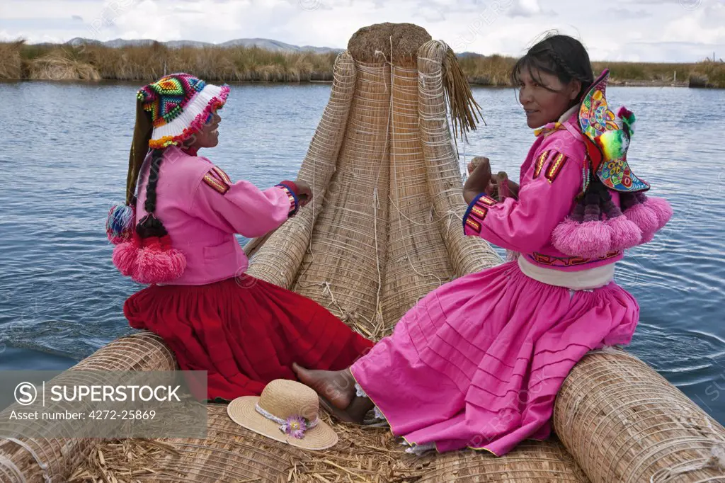 Peru, two girls from Uros row a reed boat to one of the unique floating islands of Lake Titicaca.
