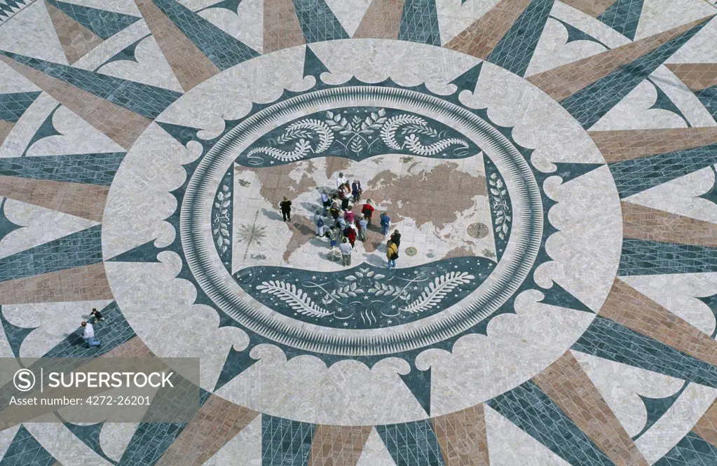 A group of tourists stand in the centre of the compass pavement in front of the Monument of the Discoveries