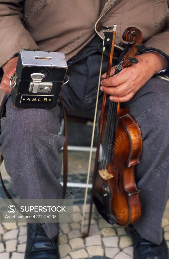 A blind street musician holds his violin in one hand and his collecting box in the other