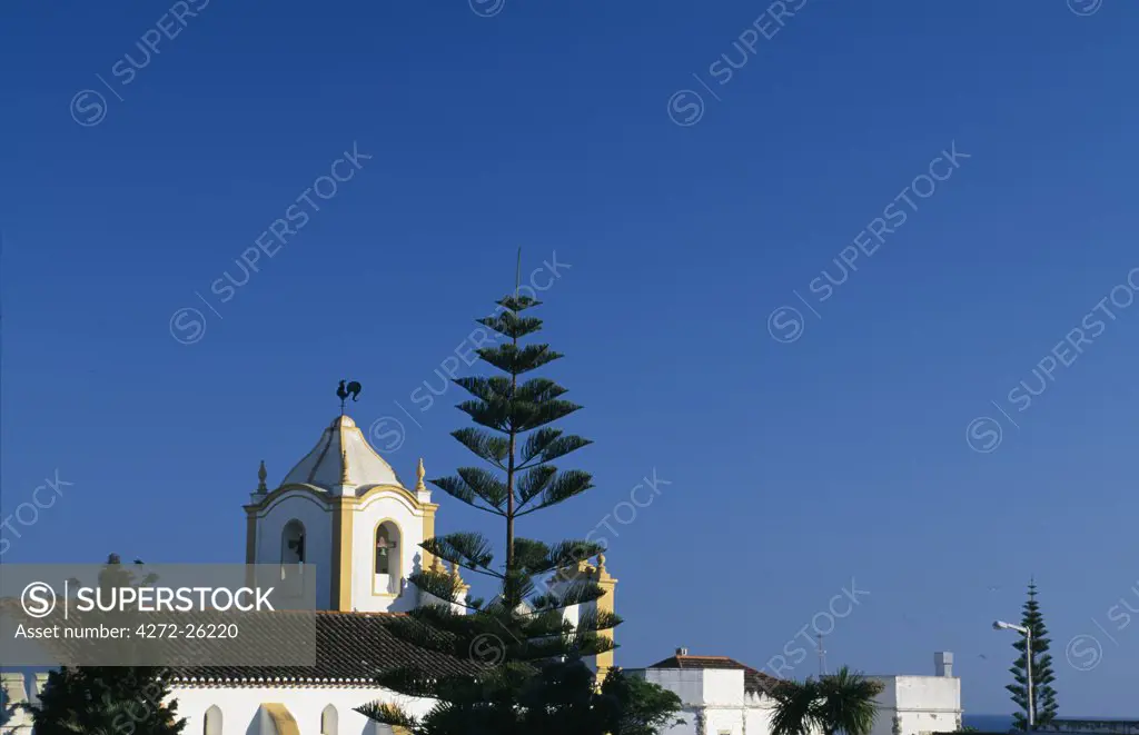 The bell tower of a whitewashed church, topped with a weathervane of a cockerel