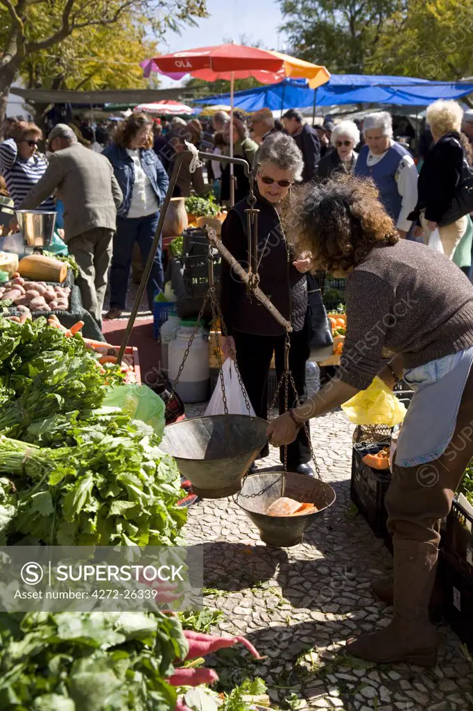 Portugal, Alentejo, Estremoz. A woman weighs some vegetables at a vegetable store at the saturday fair in the small town of Estremoz in the Alentejo region of Portugal.