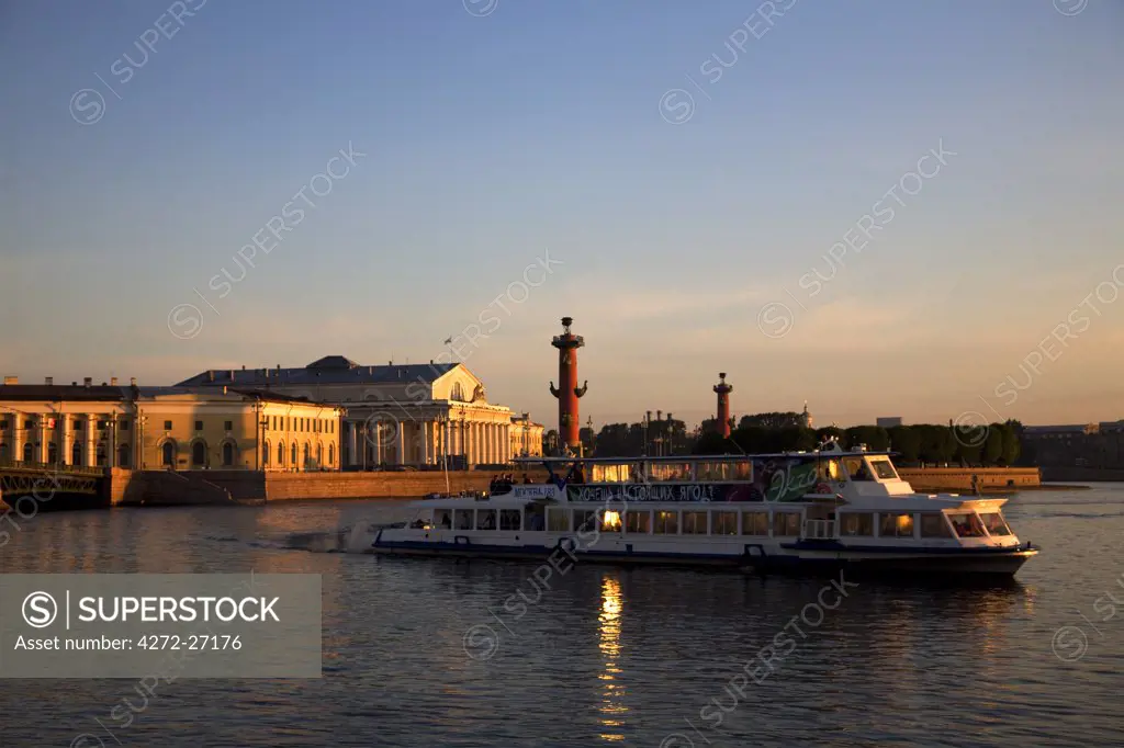 Russia, St.Petersburg; A boat at dawn crossing the Neva River with the Maritime Museum and the two Rostral Columns in the background