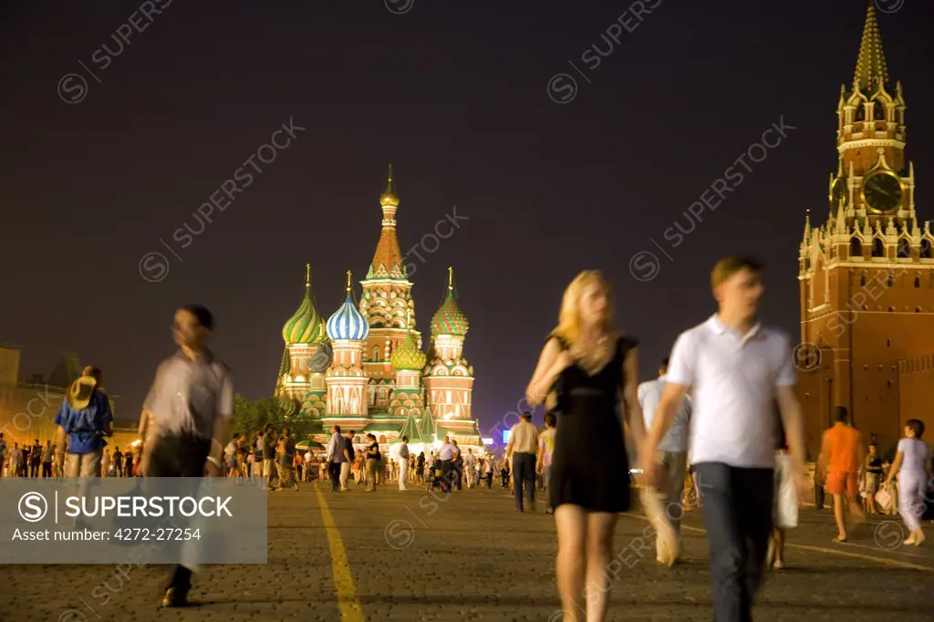 Russia, Moscow; A couple walking amidst toursits and Muscovites in Red Square, Clock Tower from the Kremlin and St.Basil's Cathedral in the background