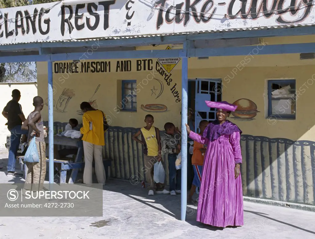 An Herero woman in traditional attire outside a restaurant and take away food business in Maun.The origins of the elaborate dress and unique hat style of Herero women can be traced back to 19th century German missionaries who took exception to what they considered an immodest form of dress among the tribe at that time.