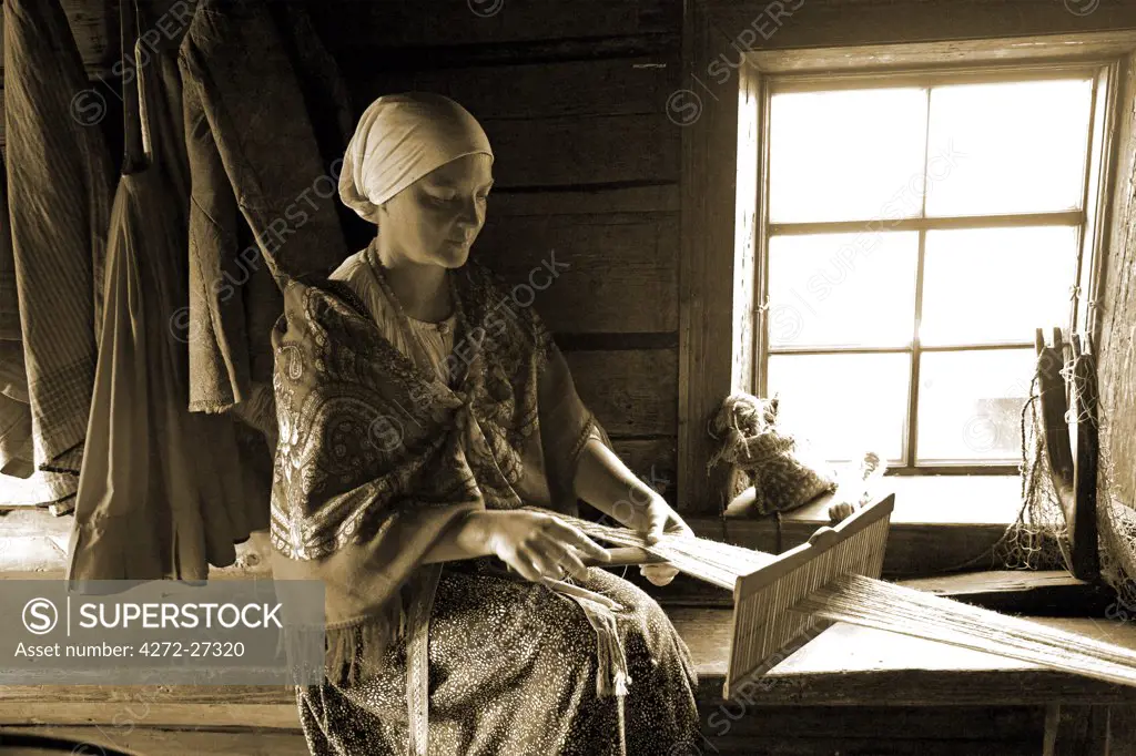 Russia; Karelia; Kizhi Island; Inside a wooden barn, a woman in a peasant costume knitting.