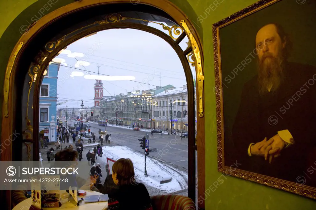 Russia, St. Petersburg; Two girls talking in a cafe with a Dostyoevski portrait on Nevski Prospekt