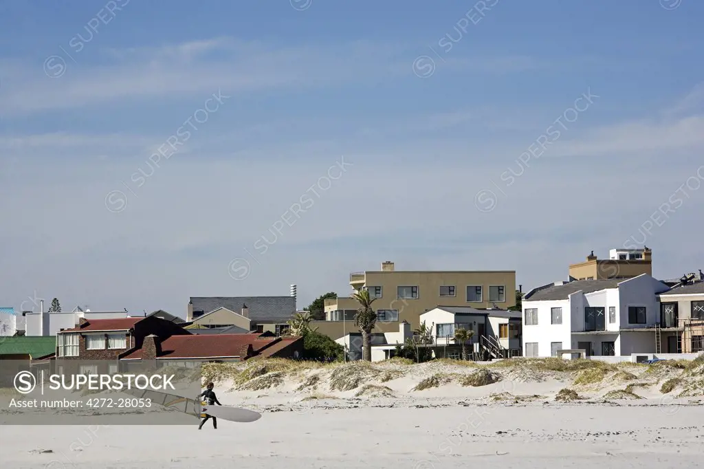 South Africa, Western Cape, Cape Town.  A wind surfer carries his board from his house to the sea for a Sunday morning surf.