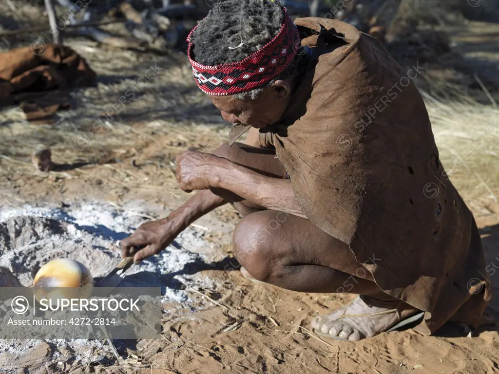 A NS hunter gatherer turns an ostrich egg in the embers of his campfire. The NS live in the harsh environment of a vast expanse of flat sand and bush scrub country straddling the Namibia Botswana border.