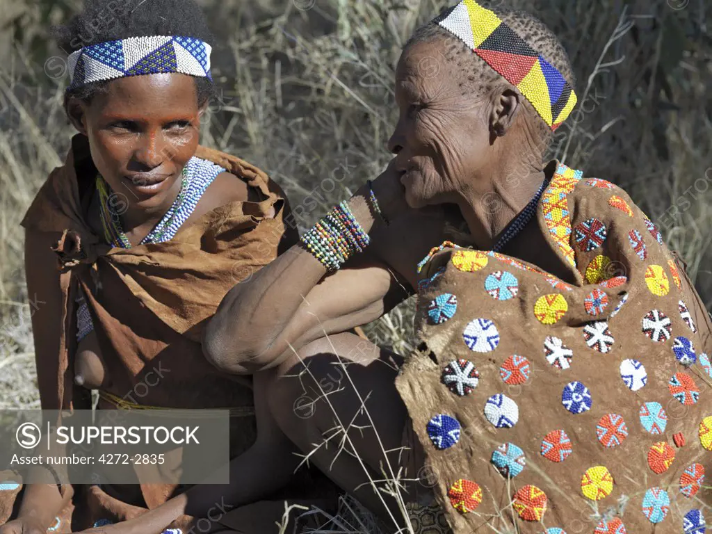 Two women from the NS hunter gatherer band talk together. The older woman is wearing a beautifully decorated leather cape. The NS live in the harsh environment of a vast expanse of flat sand and bush scrub country straddling the Namibia Botswana border.