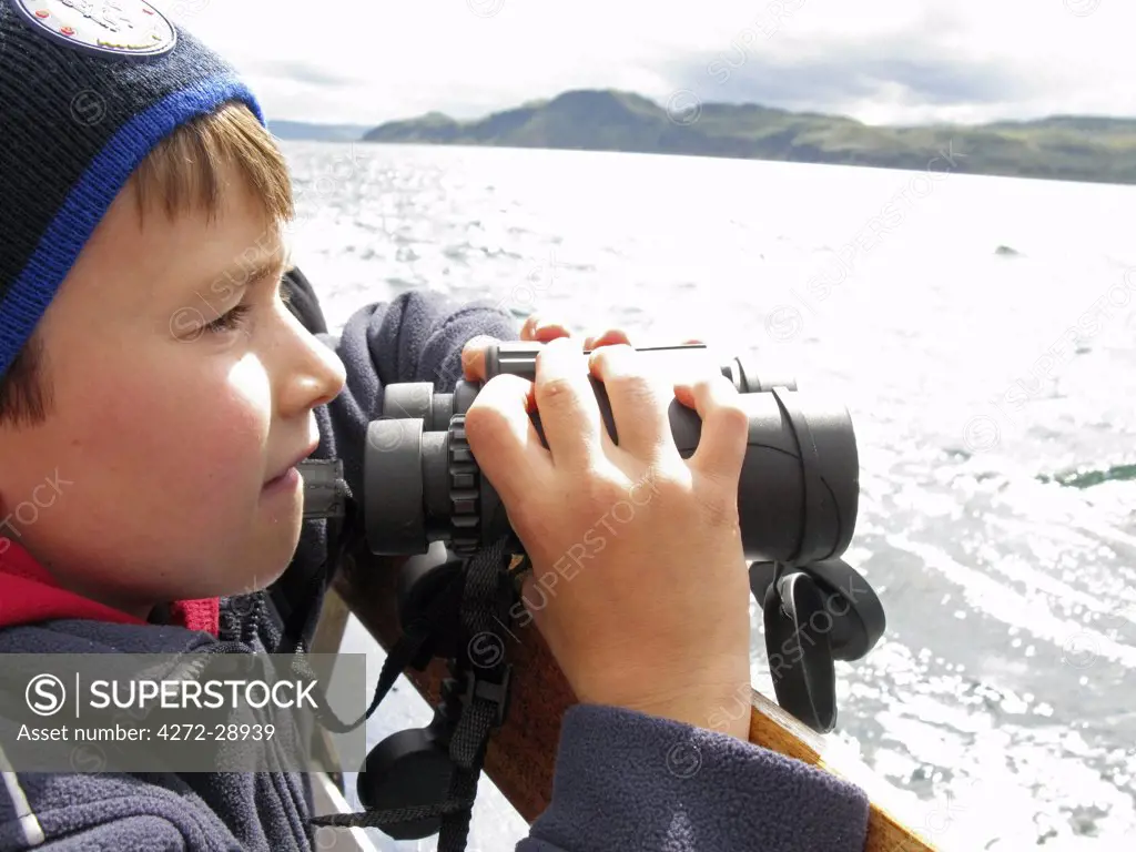 Scotland, Isle of Mull. Boy with binoculars on a whale-watching trip in the Sound of Mull. (MR)
