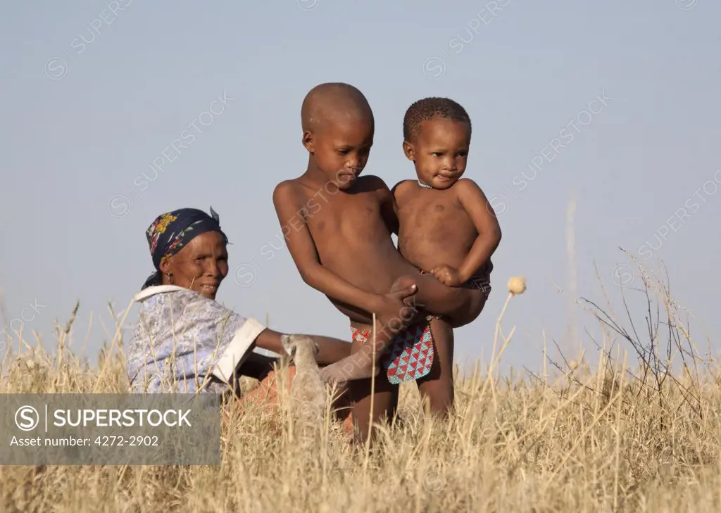 Botswana, Makgadikgadi. Bushmen children play in the dry grasses of Kalahari, watched by their mother.