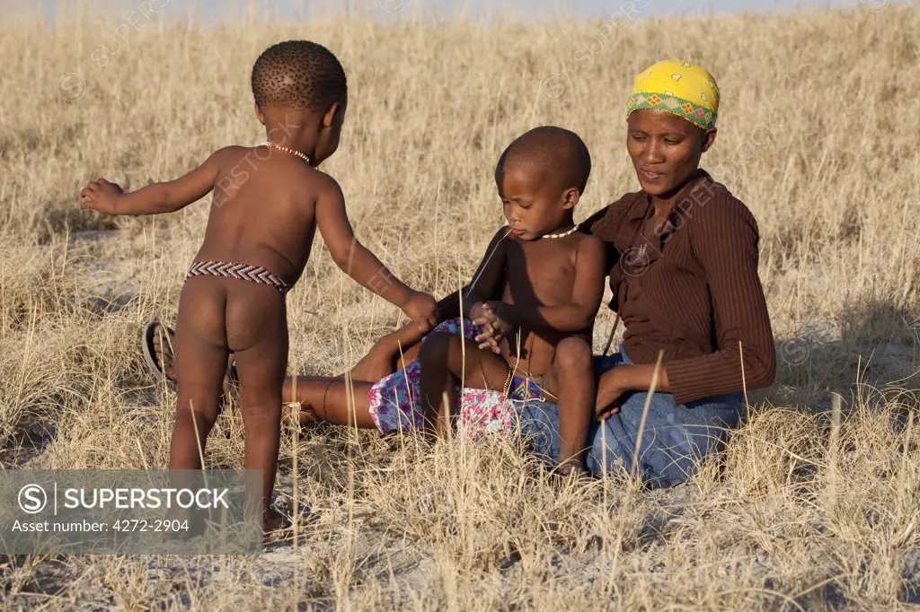 Botswana, Makgadikgadi. Bushmen children play in the dry grasses of Kalahari, watched by their mother.