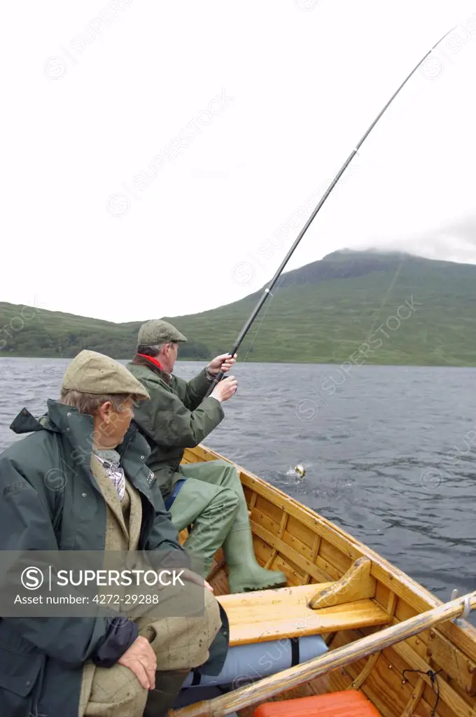 A fisherman reals in a brown trout caught on a dapping fly on Loch Ba.  Dapping is a method of salmon  and trout fishing in which a large fishing fly is made to dance over the surface of the water using a long road and length of floss which is caught by the wind and provokes the fish to take the fly