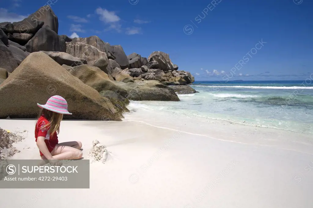 Seychelles, La Digue, Grande Anse. Girl playing on a stunning coral-sand beach with pink-granite boulders in the background. (MR)