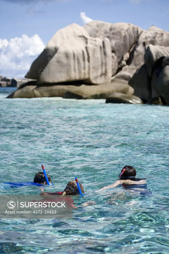 Seychelles. A mother and two children snorkel over shallow coral reefs surrounding the granite outcrops of the St Pierre Marine Park  near Praslin. (MR)