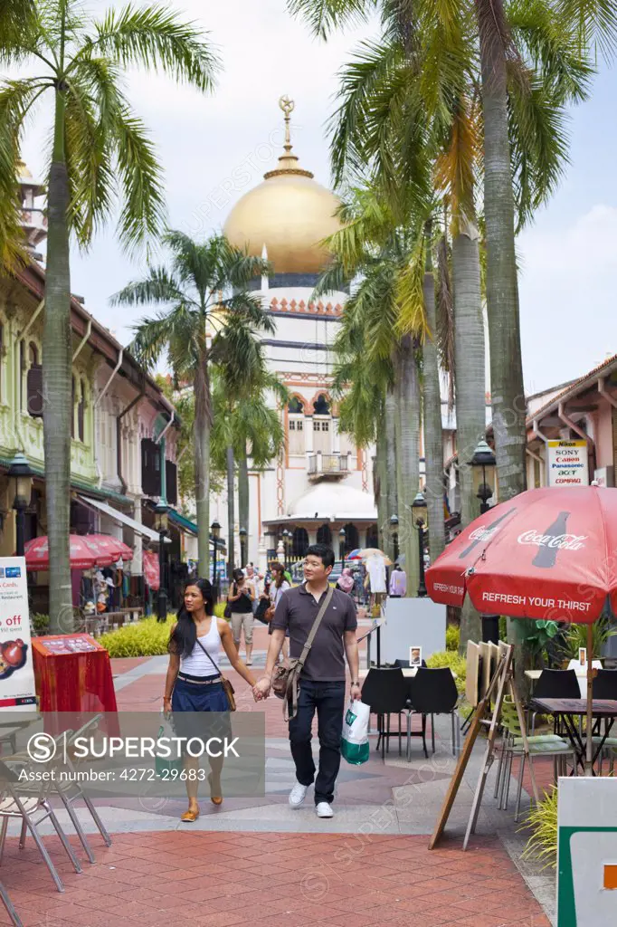 Singapore, Singapore, Arab Quarter.  Couple walking along Bussorah Mall with Sultan Mosque in background.