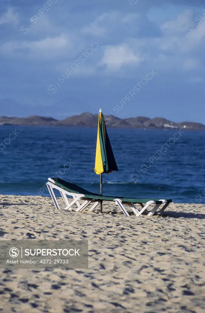 Umbrella and sun lounger on beach near Corralejo with the peaks of Lanzarote in the distance