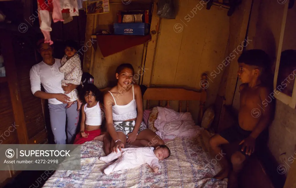 A young mother and her children sit on their bed in their simple home in a favela in Sao Paulo, Brazil.