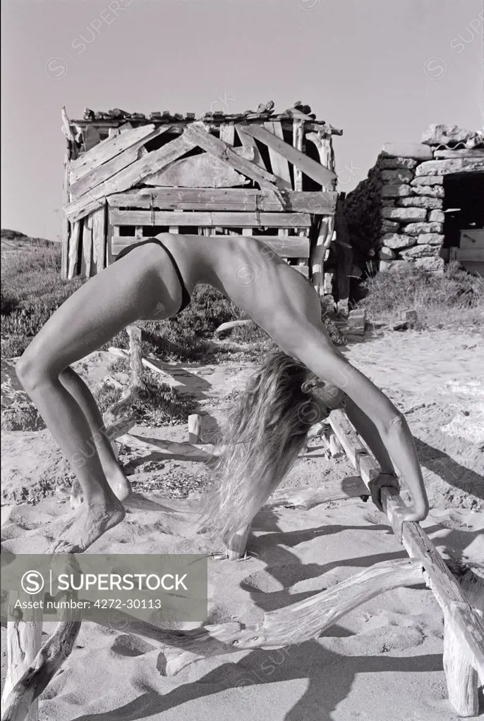 Model doing yoga the wheel/bridge chakarasana on a boat ramp on the beach