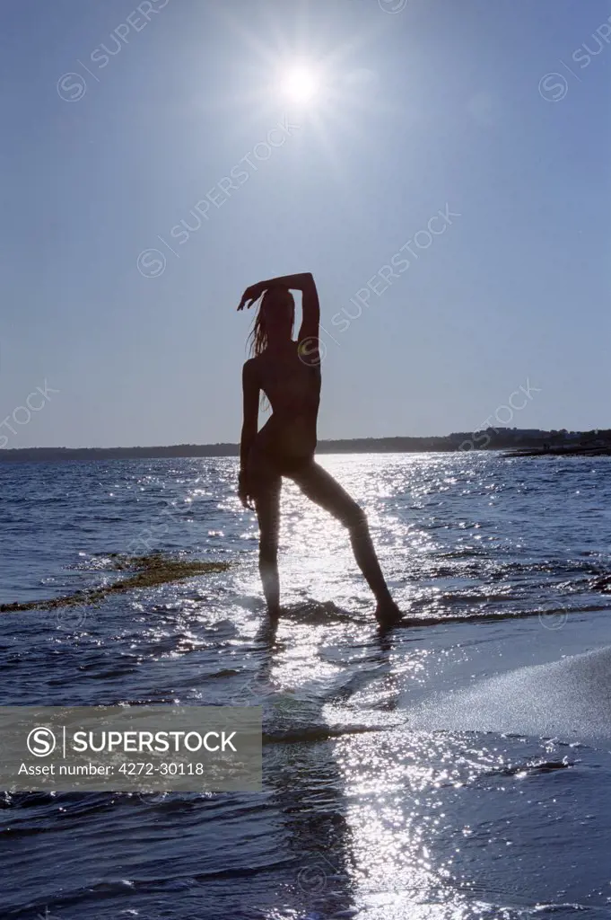 Model posing on the beach silhouetted against the setting sun