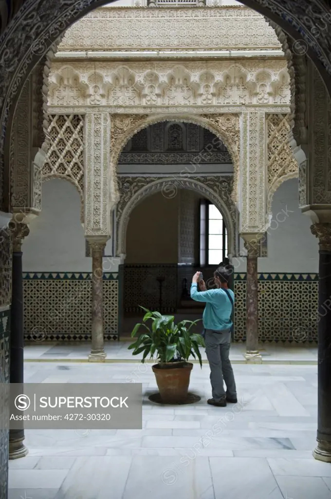 Spain, Andalucia, Seville. A tourist photographs one of the ornate courtyards inside the Alcazar Palace.