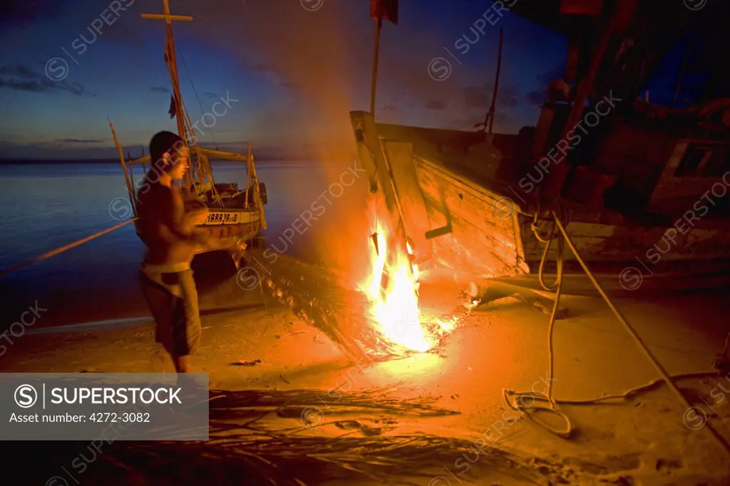 Tarring the bottom of a fishing boat during the night. The heat is used to melt and seal the tar, Tinhare archipelago in the Bahia region, north east of Brazil