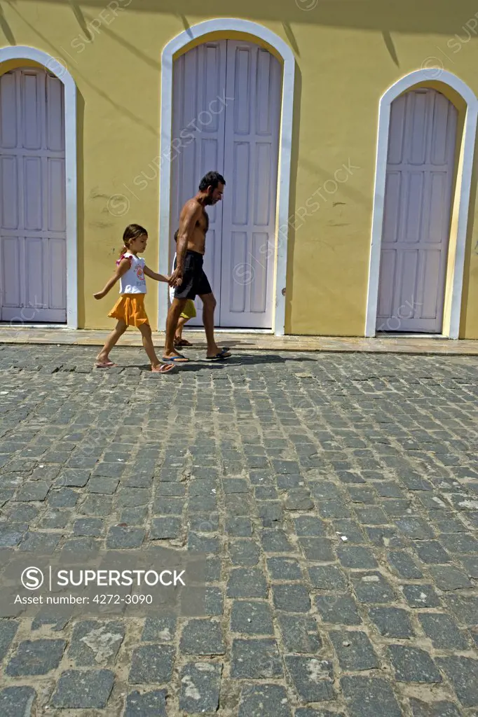 Father and daugher walk past the door to the local church on the Tinhare archipelago, Bahia, north eastern Brazil