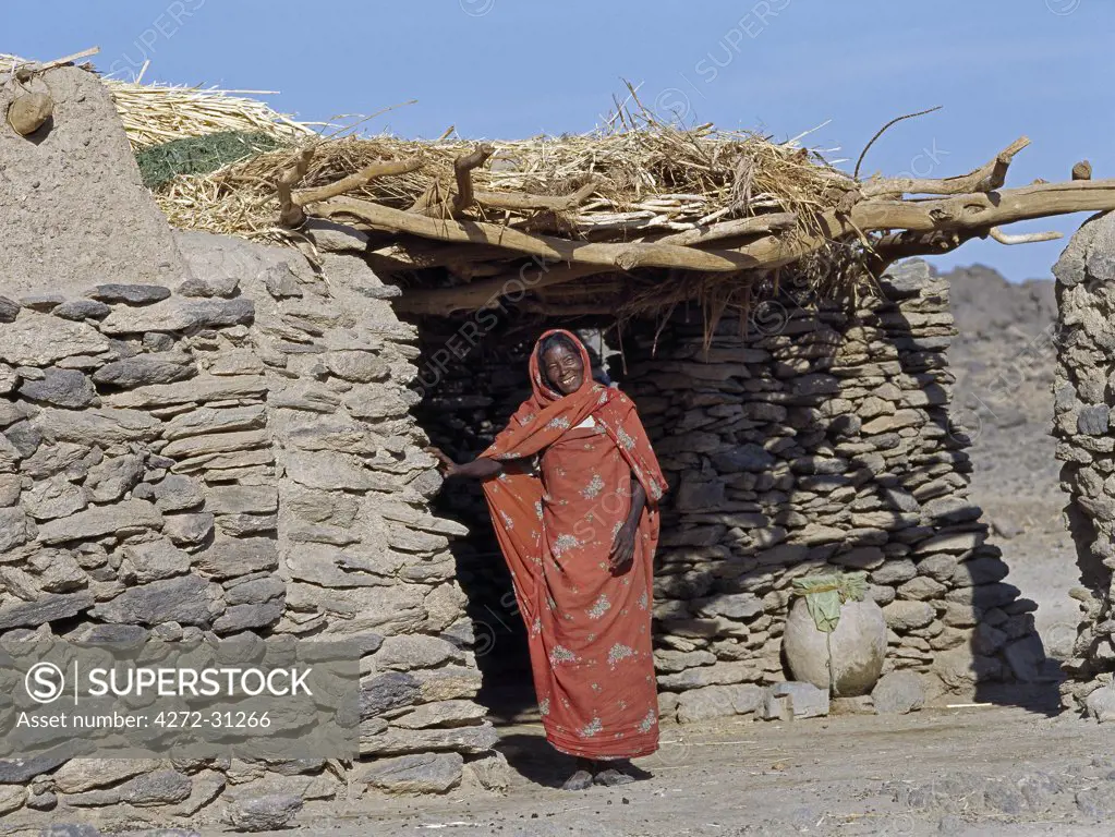 A Nubian woman stands outside her home constructed of stone with a flat earth roof.