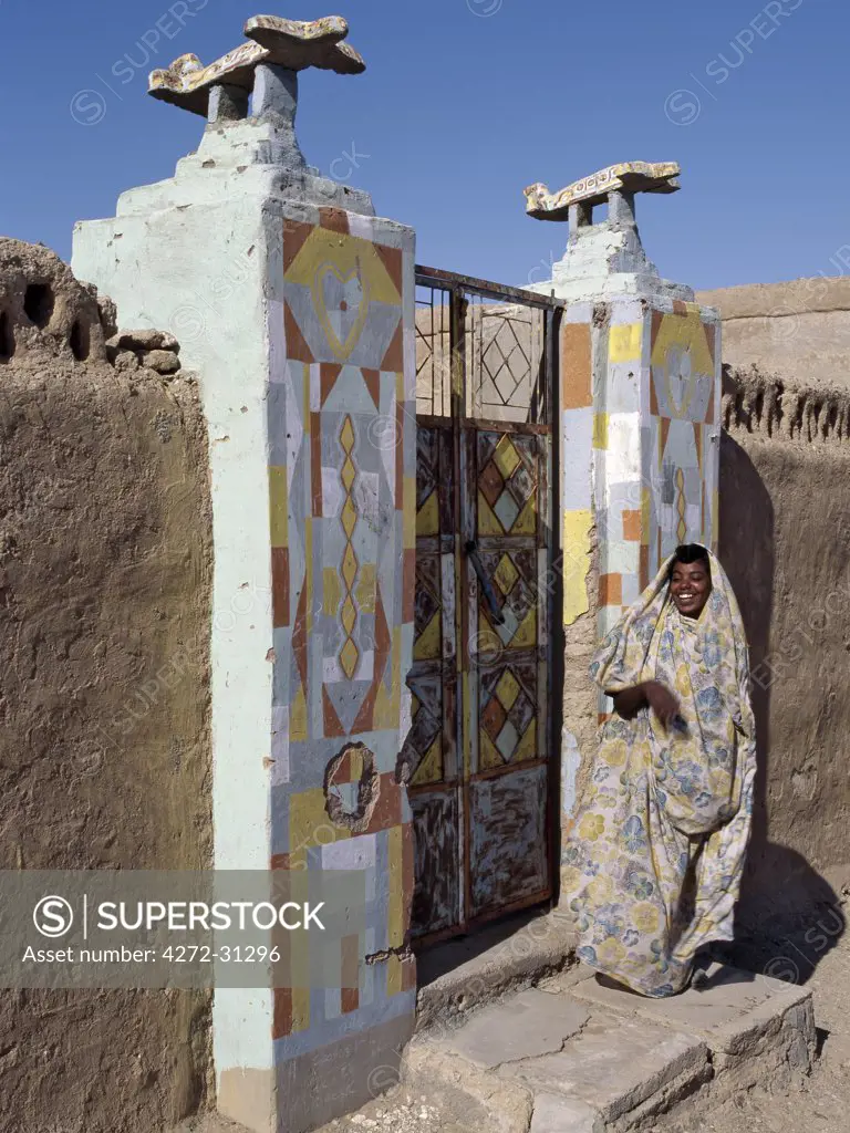 A Nubian woman stands at the entrance to her home.  The aeroplanes on these doorposts have been put there because the owner of the house has been to Mecca.  They used to put boats, but in the age of air travel the symbol has changed.